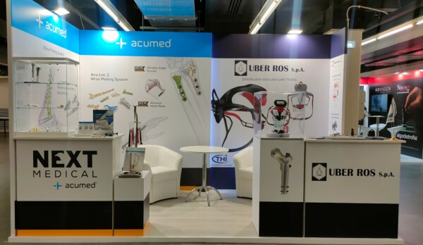 Stand Next Medical e Uber Ros Spa. Vista generale dello stand, con un'area accogliente per discussioni, l'esposizione di prodotti Next Medical e la visibilità di Uber Ros S.p.A. e dei suoi dispositivi innovativi.