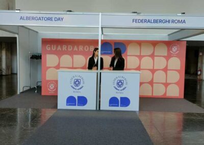 Hospitality Desk allestito da Key Comunicazione in occassione dell Albergatore Day 2025, tutto bianco a eccezione dello sfondo con il patern del logo dell'evento.