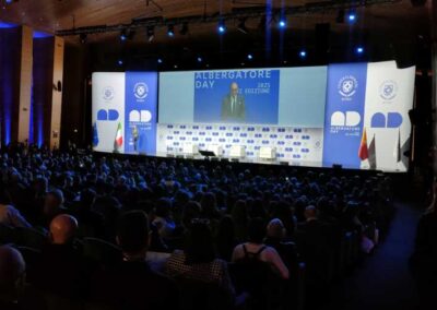 Assistenti attendono la presentazione del sindaco di Roma Walter Gualtieri sul palco dell'Albergatore Day 2025 al palazzo dei Congressi di Roma. Uno sfondo bianco e blu fa di cornice al maxischermo che progetta l'immagine amplificata del Sindaco di Roma.