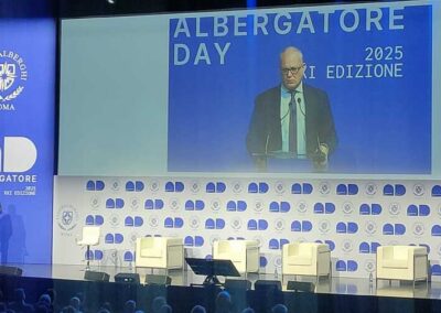 Presentazione del sindaco di Roma Walter Gualtieri sul palco dell'Albergatore Day 2025 al palazzo dei Congressi di Roma. Uno sfondo bianco e blu fa di cornice al maxischermo che progetta l'immagine amplificata del Sindaco di Roma.