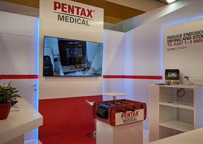 Progettazione Stand Aziendale per Congresso Medico con Key Comunicazione. Scopri il progetto Pentax e contattaci per il tuo evento. per lo stand Pentax Medical al Congresso FISMAD progettato da Key Comunicazione. Focus centrale sul grande schermo a parete con contenuti dinamici, affiancato da dispositivi endoscopici e una libreria bianca per l’esposizione. In primo piano spicca un calcio balilla personalizzato con il logo dell’azienda, un dettaglio conviviale pensato per stimolare l’interazione informale. L’ambiente combina linee pulite, illuminazione fredda e accenti rossi per rafforzare l’identità visiva dello stand