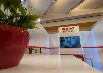 Progettazione Stand Aziendale per Congresso Medico con Key Comunicazione. Scopri il progetto Pentax e contattaci per il tuo evento. Lo stand Pentax Medical al Congresso FISMAD firmato da Key Comunicazione. Inquadratura prospettica dall’interno dello stand, con una pianta verde in primo piano su una superficie bianca lucida. Sullo sfondo, il monitor centrale trasmette contenuti digitali, incorniciato da pannelli retroilluminati. Le linee geometriche dello spazio, i colori coerenti con il brand e la luce diffusa creano un’atmosfera ordinata e professionale. Un esempio concreto di exhibit design orientato all’esperienza del visitatore.
