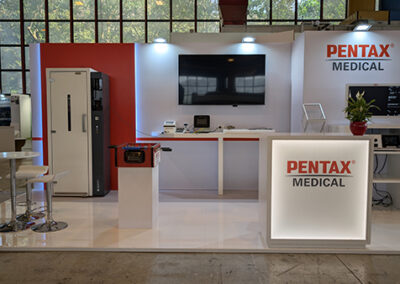 Vista frontale dello stand Pentax Medical all’AIIC di Napoli 2025 realizzato da Key Comunicazione, con banco reception illuminato, monitor centrale e arredi tecnici.