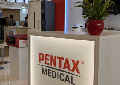 Dettaglio del banco reception retroilluminato dello stand Pentax Medical all’AIIC di Napoli 2025 progettato da Key Comunicazione, con pianta ornamentale in primo piano.