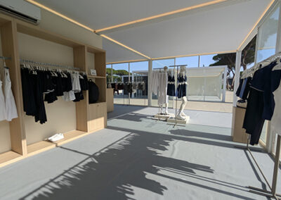 Panoramica laterale dello stand Oysho progettato da Key Comunicazione: espositori a parete con abbigliamento bianco, nero e neutro; manichini centrali e vetrate perimetrali che fondono interno ed esterno in continuità visiva. Design minimal e arioso.