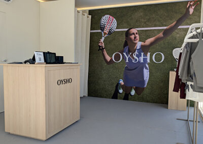 Focus sull’area cassa con brand wall “Oysho” realizzata da Key Comunicazione. In primo piano un bancone in legno chiaro e sullo sfondo una gigantografia con atleta in azione, elemento scenografico che comunica energia sportiva e immersione nel contesto padel.