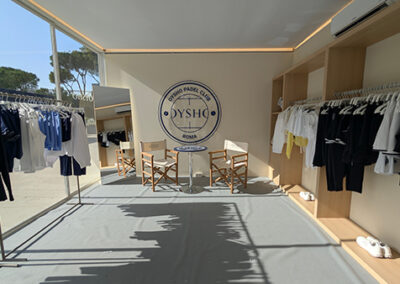 Area lounge dello stand Oysho progettato da Key Comunicazione al BNL Italy Major Premier Padel 2025. Vista centrale dell’area relax con sedute da regista e parete brandizzata “Oysho Padel Club Roma”. Espositori lineari in legno chiaro ai lati con abbigliamento sportivo ordinato per cromia.
