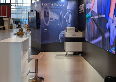 Vista interna dello stand Storz all’AIIC di Napoli 2025, a cura di Key Comunicazione: monitor, stampante, grafiche scure e seduta per consulenza tecnica.
