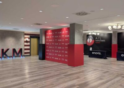 Allestimento Enovis Roma per il Knee Kinematics Meeting: desk di registrazione rosso e nero con logo K.K.M. tridimensionale, Hotel Villa Pamphili. Una Hall con colunne e pareti allestite con i colori ufficiali della Enovis (Rosso, nero, griggio chiaro) si sono delle lettere in gigantografia rappreentando le sigle KKM.