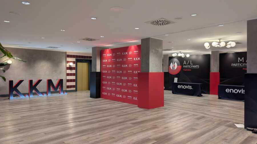 Allestimento Enovis Roma per il Knee Kinematics Meeting: desk di registrazione rosso e nero con logo K.K.M. tridimensionale, Hotel Villa Pamphili. Una Hall con colunne e pareti allestite con i colori ufficiali della Enovis (Rosso, nero, griggio chiaro) si sono delle lettere in gigantografia rappreentando le sigle KKM.