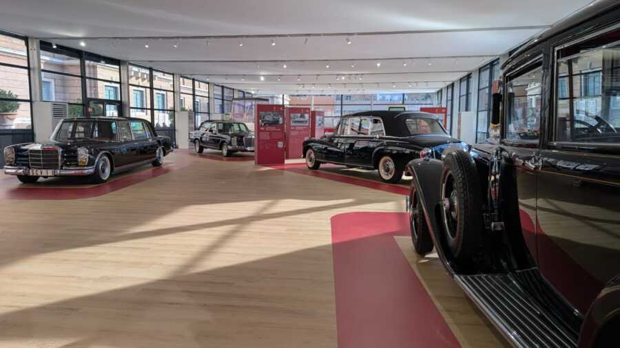 Allestimento Mercedes-Benz Musei Vaticani con esposizione di auto storiche, pannelli informativi rossi e percorso espositivo.