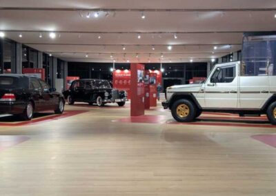 Allestimento Mercedes-Benz Musei Vaticani con vetture storiche e moderne, pavimentazione effetto legno e illuminazione a faretti.