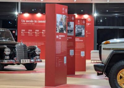 Esposizione Mercedes-Benz con vetture storiche, percorso grafico rosso e pannelli informativi all'interno dello spazio espositivo.