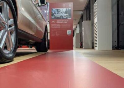 Dettaglio del percorso espositivo Mercedes-Benz con pavimentazione rossa, pannelli descrittivi e illuminazione a binario.
