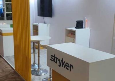 Area incontri dello stand Stryker con tavolo alto e sgabelli sotto il portale giallo, congresso SINch di Catania