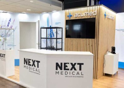 Bancone accoglienza Next Medical davanti al volume in legno listellare con logo Acumed e monitor, Trauma Meeting di Riccione