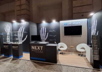 Stand Next Medical e Acumed in versione scura con teche illuminate e grafiche dedicate a mano e polso, allestito da Key Comunicazione a Verona