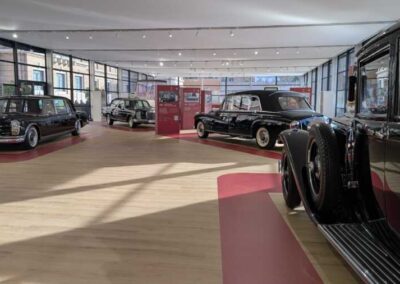 Allestimento “Un secolo di Papamobile” alla luce del giorno: Papamobili Mercedes-Benz lungo un percorso rosso su parquet
